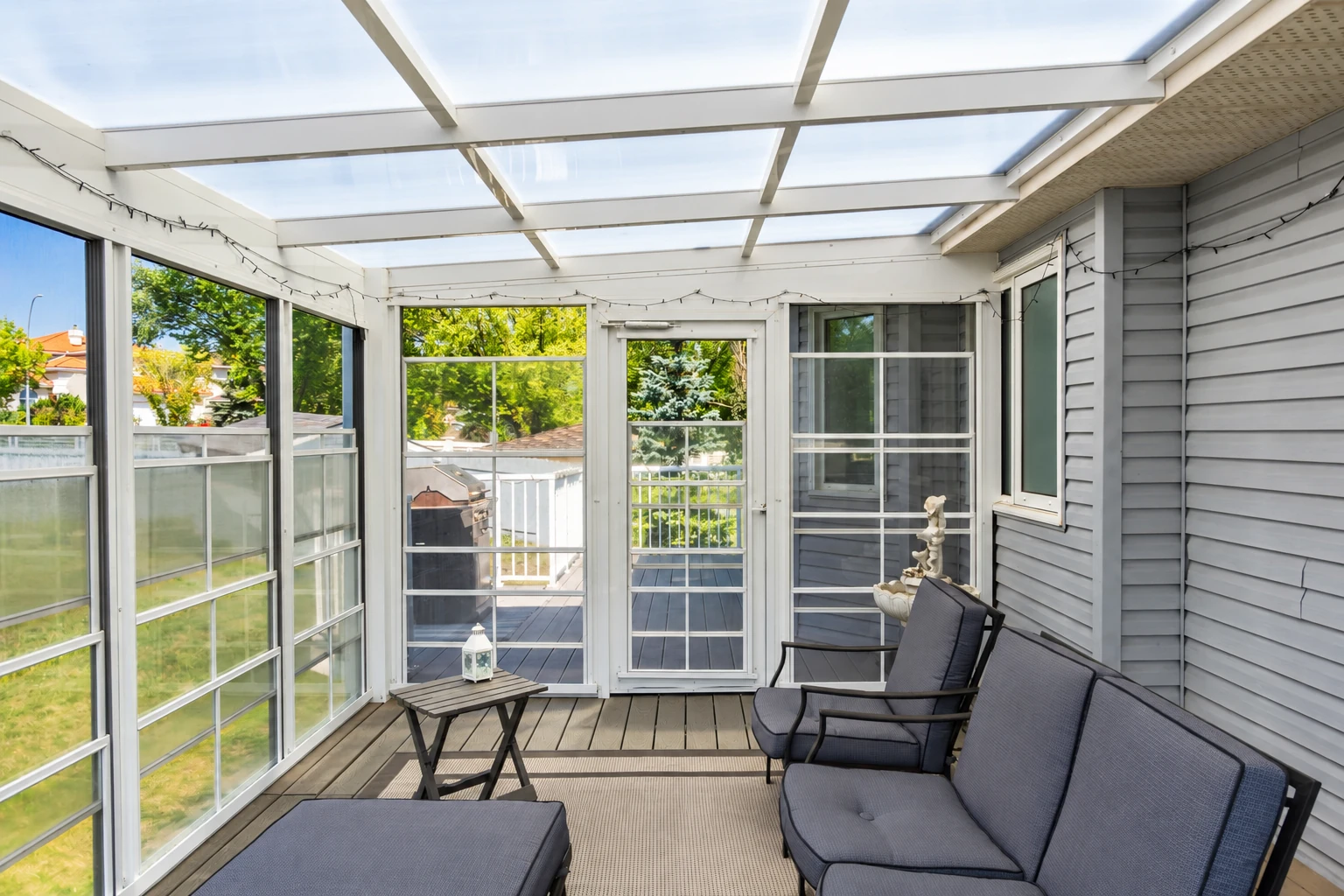 Enclosed patio with a translucent roof, screened windows, gray siding and cushioned seating.