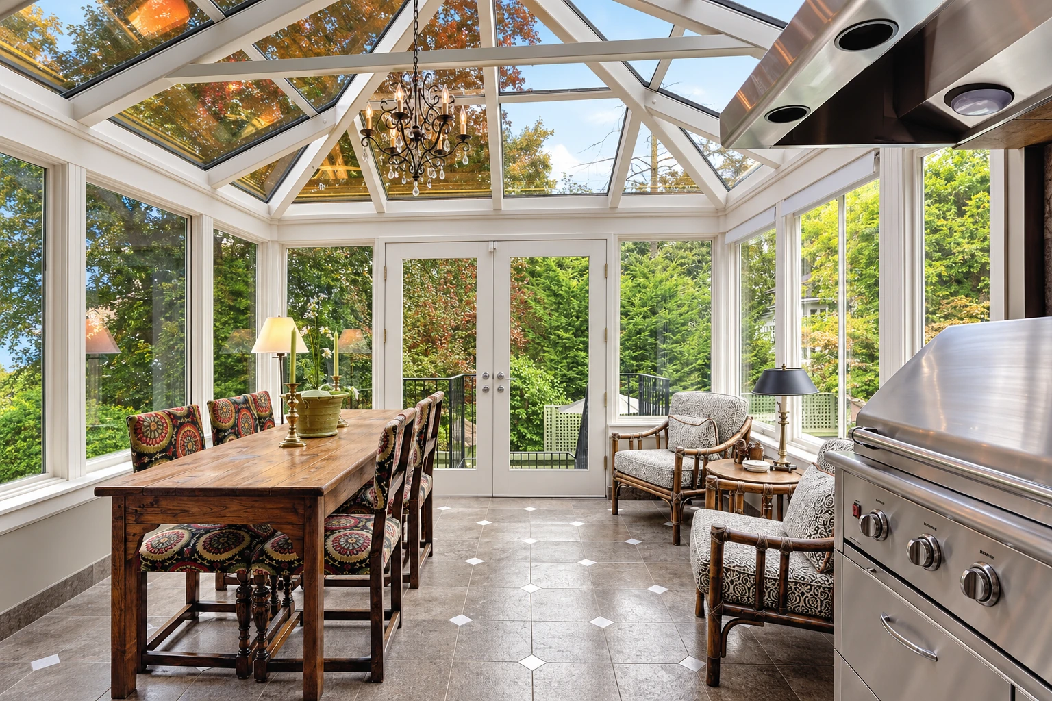 A glass solarium with a peaked skylight has a wooden dining table, upholstered chairs, and a stainless-steel grill.