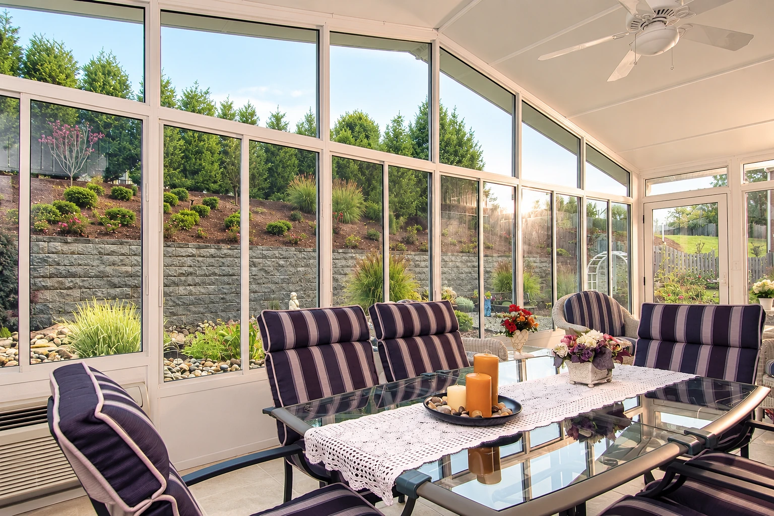 Bright sunroom with floor-to-ceiling windows, a glass dining table, and purple-striped seating overlooking a landscaped garden.